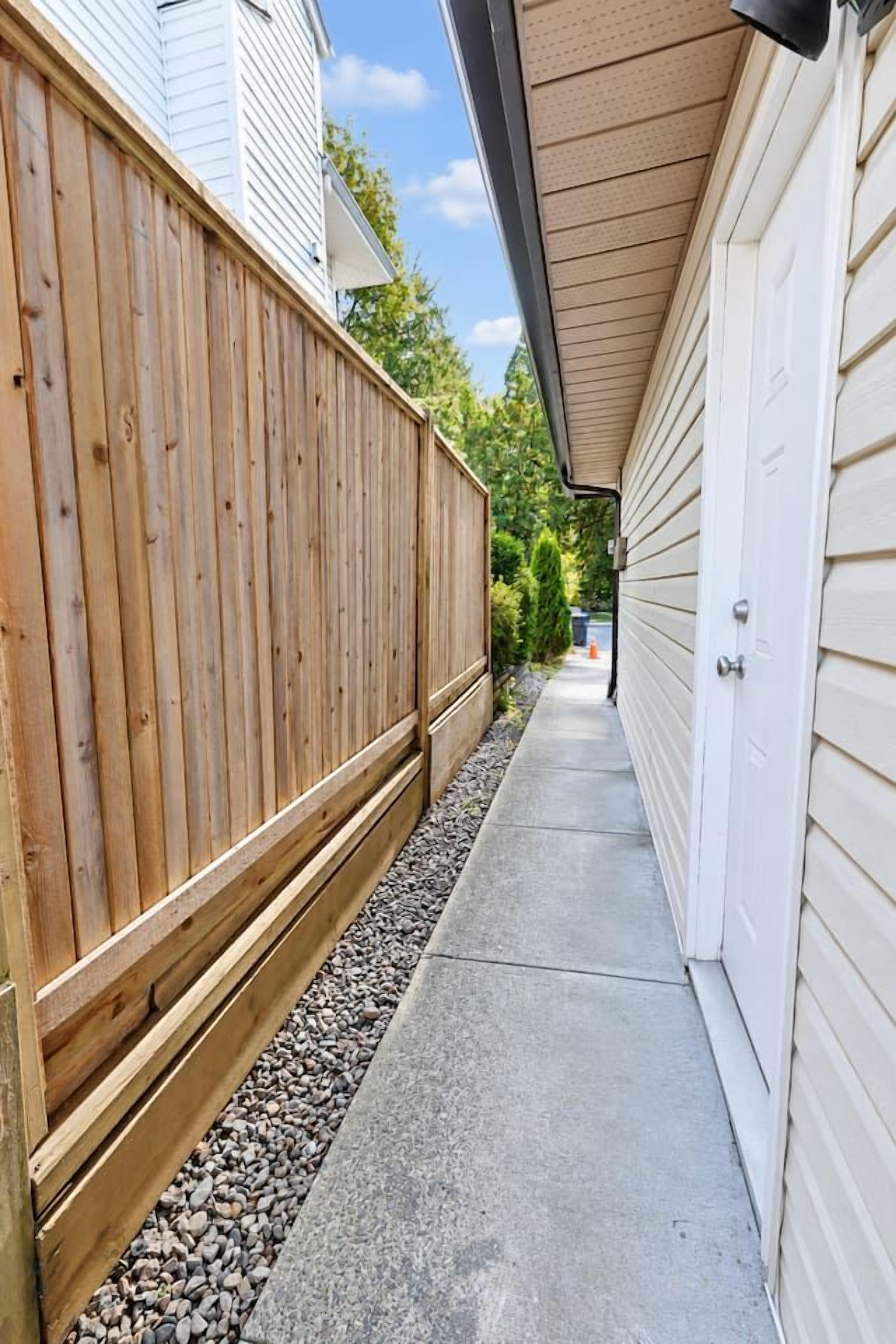 A narrow concrete pathway flanked by a wooden fence and a building with a garage door.