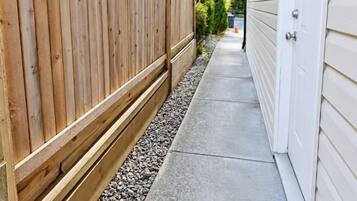 A narrow concrete pathway flanked by a wooden fence and a building with a garage door.