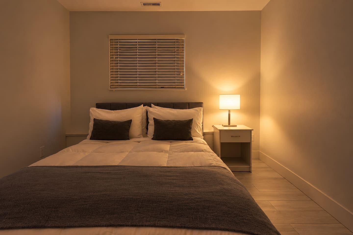A bedroom with a bed, bedside table, lamp, and window blinds.