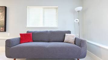 A grey sofa with two cushions, a floor lamp, and a window with blinds.
