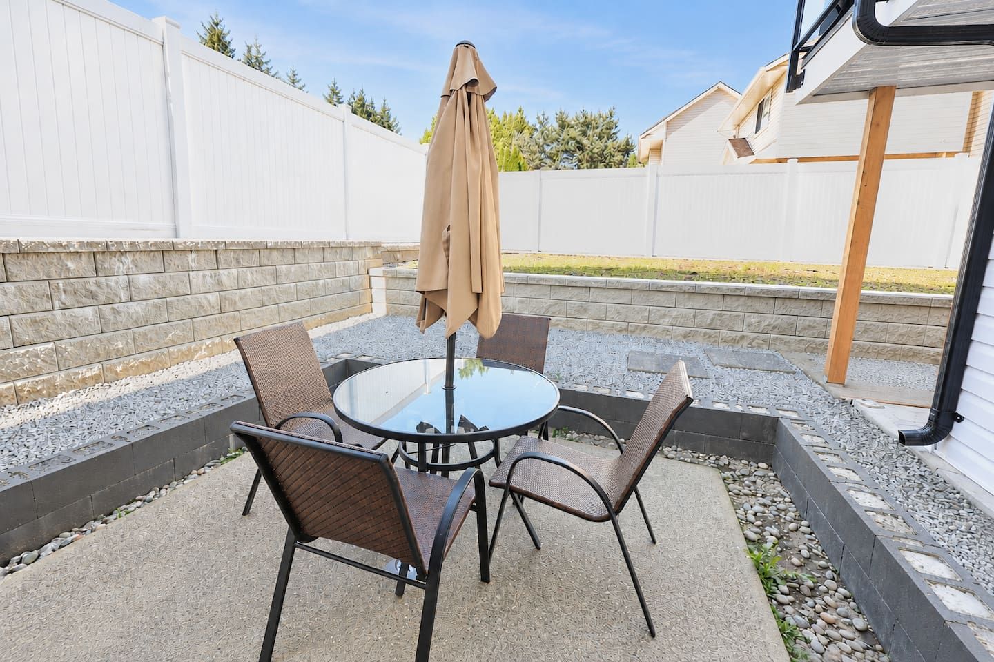 A round table with four chairs and a single umbrella in a backyard patio area.