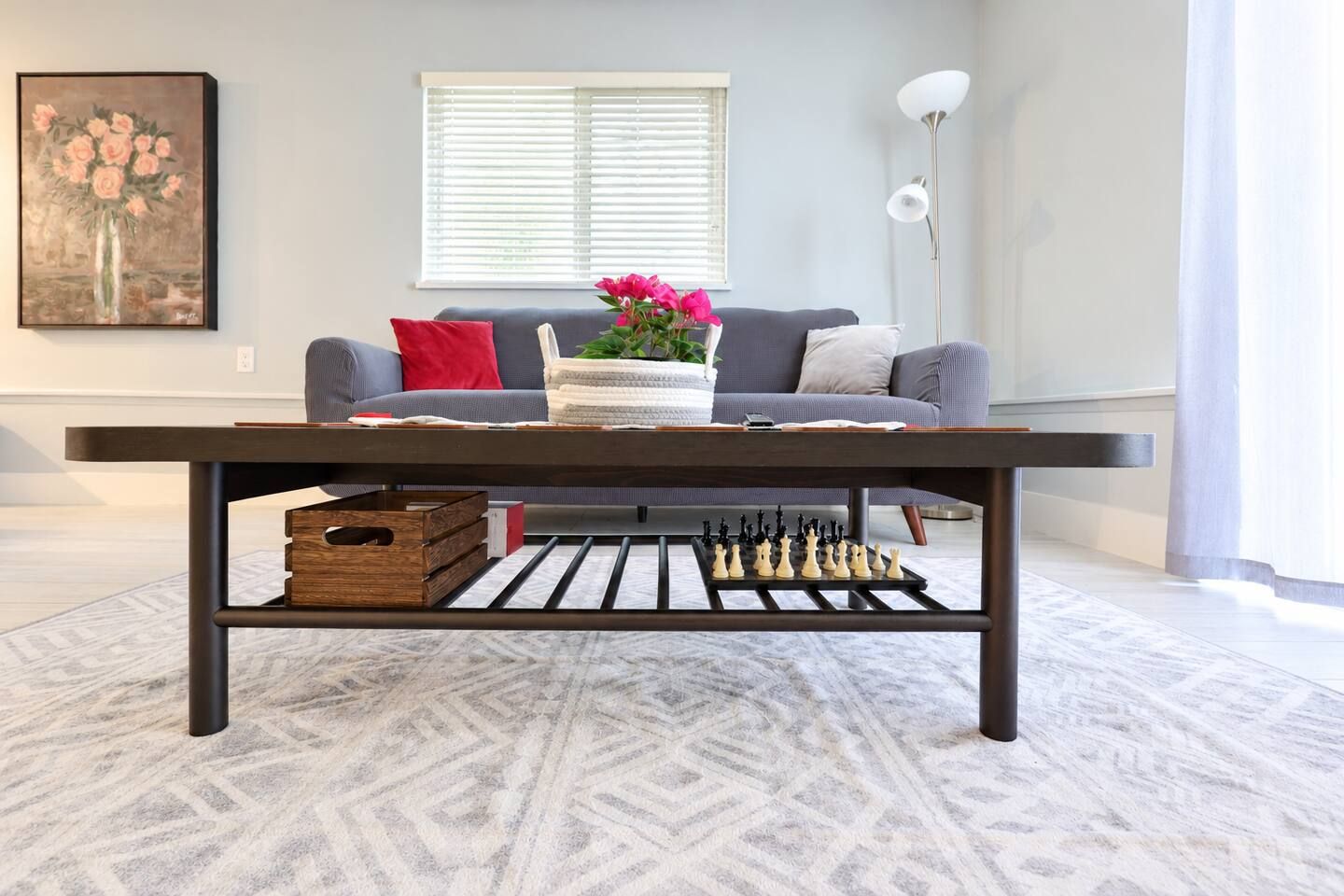 A living room with a dark wooden coffee table, a sofa with cushions, a vase with flowers, and a chessboard on the table.