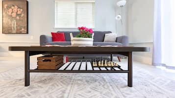 A living room with a dark wooden coffee table, a sofa with cushions, a vase with flowers, and a chessboard on the table.