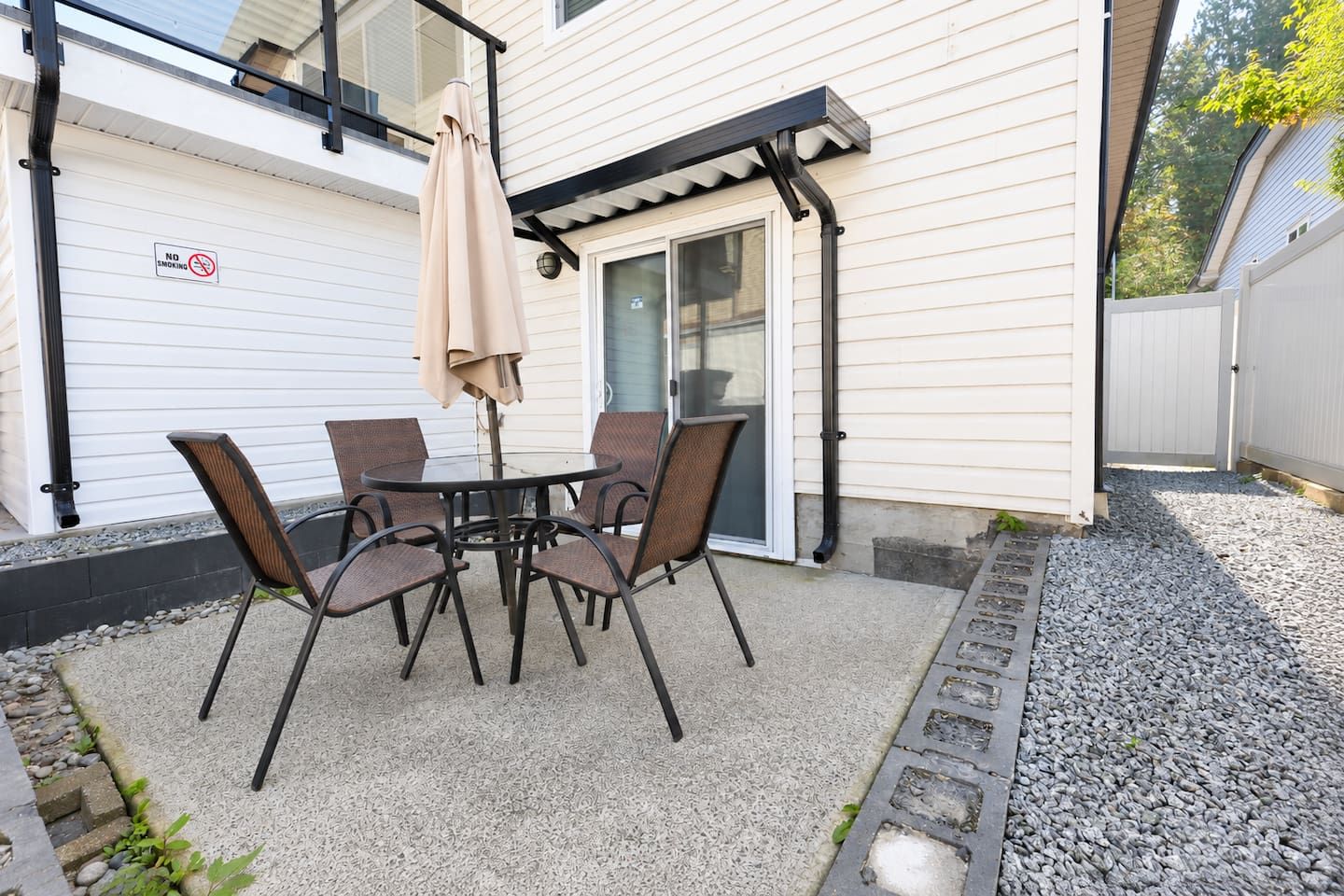 Eine Terrasse mit Tisch und Stühlen, einem schattenspendenden Sonnenschirm und einem Rauchverbot-Schild an der Wand.