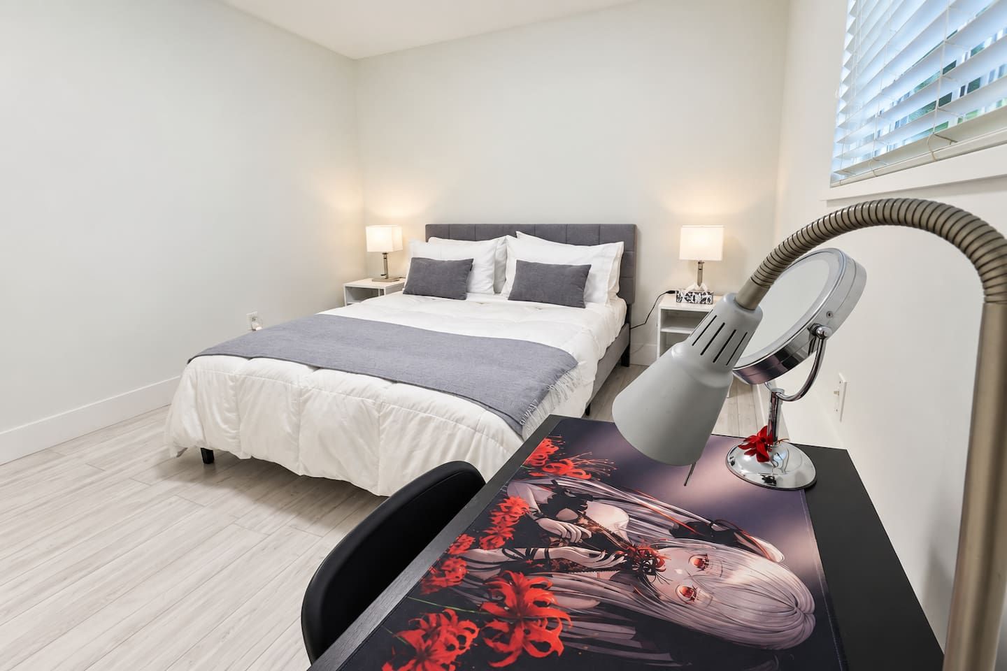 A bedroom with a bed, bedside tables, a desk with a lamp, and a poster.
