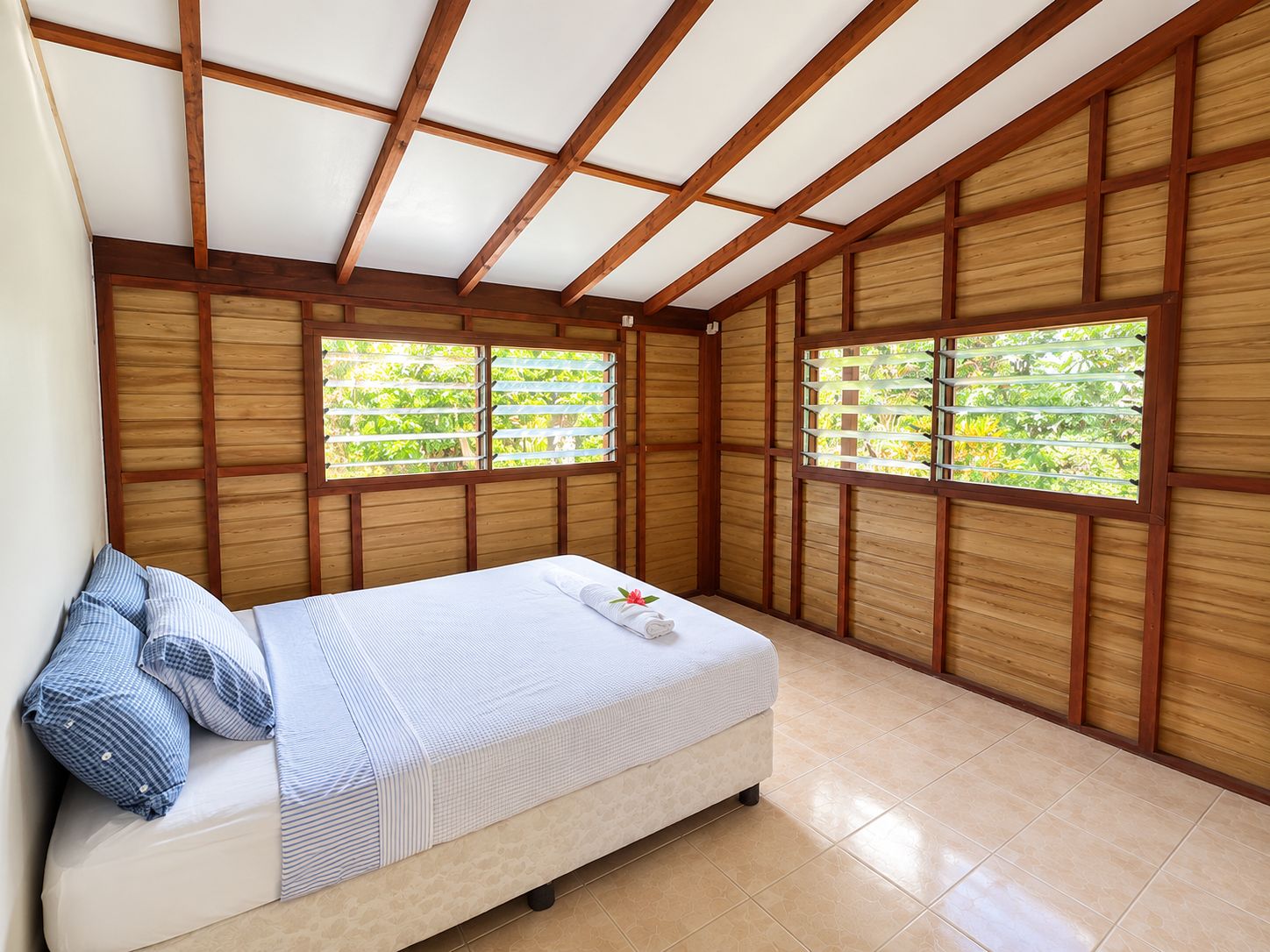 A room with a bed, wooden walls, and windows with blinds.