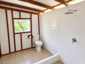 A bathroom with a toilet, a shower, and a window with a view of greenery. - Freshwater Plantation Family Cottage (Canal - Fanafo)