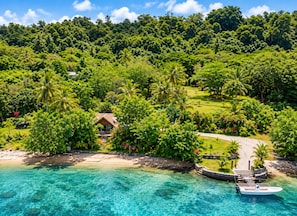 A tropical resort with a beachfront, clear waters, and lush greenery.