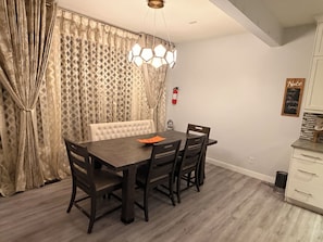 Un coin repas avec une table en bois foncé, six chaises, un banc capitonné, un luminaire suspendu à six faces et un extincteur fixé au mur.