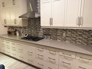 A modern kitchen with a stainless steel range hood, a tiled backsplash, and a built-in oven. - Nolan Hill Mountain Gateway | Spacious 4BR Home (Calgary)