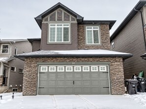 A two-story house with a stone facade, a garage with multiple doors, and a snow-covered roof. - Nolan Hill Mountain Gateway | Spacious 4BR Home (Calgary)