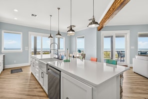 A modern kitchen with a large island, pendant lighting, and a view of the ocean through large windows. - A Sight for Shore Eyes: Beachfront Home, Sleeps 10 (Port Aransas)