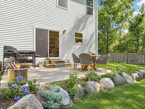 Ein Haus mit einer Terrasse, inklusive Grill, Gartenmöbeln und einem Feuerkorb.