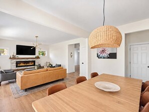 Ein modernes Wohnzimmer mit Kamin, einer großen Couch, einem Esstisch mit Stühlen und einer Pendelleuchte.