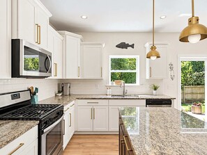 A modern kitchen with white cabinets, a stainless steel range, a built-in microwave, and a granite countertop. - Lakeshore Retreat | Hot Tub • 5BR • Steps to Beach (South Haven)