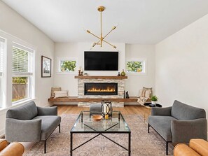 A modern living room with a fireplace, a flat-screen TV, and two grey sofas. - Lakeshore Retreat | Hot Tub • 5BR • Steps to Beach (South Haven)
