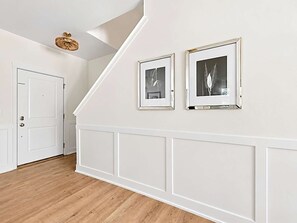 A hallway with white walls, a wooden floor, and two framed pictures. - Lakeshore Retreat | Hot Tub • 5BR • Steps to Beach (South Haven)