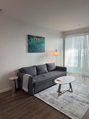 A modern living room with a grey sofa, a round coffee table, a small side table, and a painting on the wall. - Elegant 1-bedroom apartment in Marina del Rey (Marina del Rey)