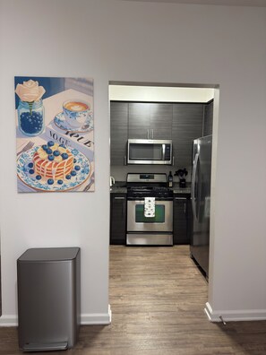 A modern kitchen with stainless steel appliances, a wooden floor, and a wall-mounted artwork. - Elegant 1-bedroom apartment in Marina del Rey (Marina del Rey)