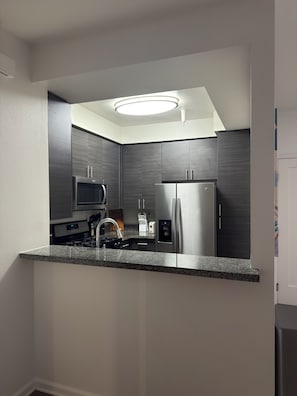 A modern kitchen with a built-in microwave, stainless steel refrigerator, granite countertop, and a ceiling light fixture. - Elegant 1-bedroom apartment in Marina del Rey (Marina del Rey)