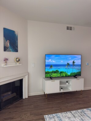 A living room with a flat-screen TV, white entertainment unit, fireplace, and a painting on the wall. - Elegant 1-bedroom apartment in Marina del Rey (Marina del Rey)