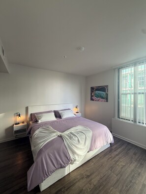 A bedroom with a bed, two bedside tables with lamps, a window with blinds, and a painting on the wall. - Elegant 1-bedroom apartment in Marina del Rey (Marina del Rey)
