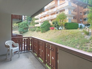 A balcony with a view of a residential building, a white plastic chair, and a wooden fence. - Domino B 38 by Interhome (Ovronnaz)