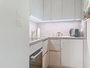 A compact kitchen with a built-in oven, a coffee maker, and a kettle on the countertop. - Domino B 38 by Interhome (Ovronnaz)