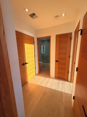 A hallway with wooden doors leading to a bathroom with a glass shower enclosure. - The Panorama Beach House (Wailuku)