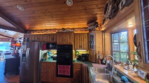 L’intérieur d’une cabane en bois comprend un coin cuisine équipé de meubles de rangement en bois, d’un réfrigérateur, d’un four à micro-ondes et d’un évier.