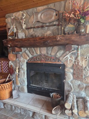 A stone fireplace with a wooden mantel, surrounded by various decorative items including a fish skeleton, a vase with flowers, and a woven basket. - Pine Beach Peninsula iconic property on Gull Lake. Truly one of a kind & special (City of East Gull Lake)