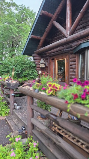 A log cabin with a wooden porch, a metal bucket, and potted plants. - Pine Beach Peninsula iconic property on Gull Lake. Truly one of a kind & special (City of East Gull Lake)