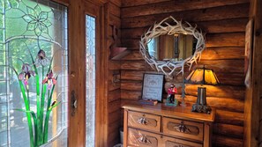 A wooden cabin interior with a stained glass window, a mirror, a dresser, and a wall-mounted lamp. - Pine Beach Peninsula iconic property on Gull Lake. Truly one of a kind & special (City of East Gull Lake)