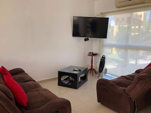 A living room with two brown sofas, a flat-screen TV mounted on the wall, a small table, and a standing fan. - Casa Diamante: private pool, paddle court, 24/7 security (Acapulco de Juárez)