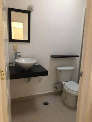 Ein kleines Badezimmer mit einem weißen Waschbecken, einer Toilette und einem schwarzen Regal darüber.