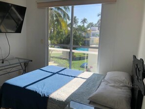 A bedroom with a bed, a TV mounted on the wall, and a view of a swimming pool and palm trees through a sliding glass door. - Casa Diamante: private pool, paddle court, 24/7 security (Acapulco de Juárez)