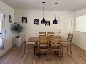 A dining area with a wooden table and chairs, black pendant lights, and wall art featuring coffee themes. - Echo Valley Retreat: Hot Tub, Game Room & Views near Yosemite (Oakhurst)