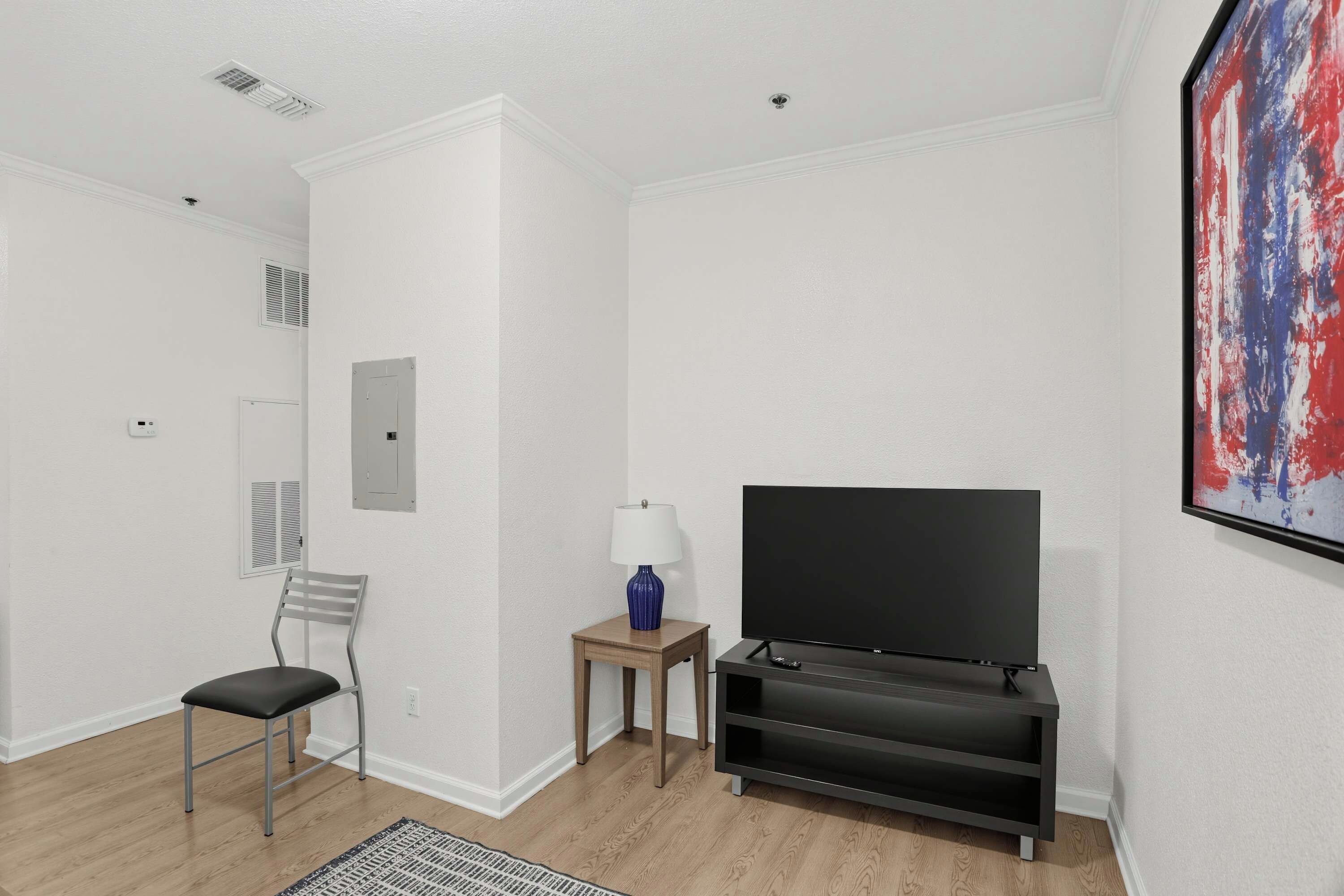 Een moderne woonkamer met een flatscreen televisie, een stoel, een klein tafeltje met een lamp en een schilderij aan de muur.