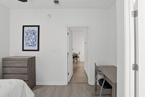 Un dormitori amb un llit, una petita arca, un escriptori i una cadira. Hi ha una porta que dóna a una zona de dinar amb taula i cadires.