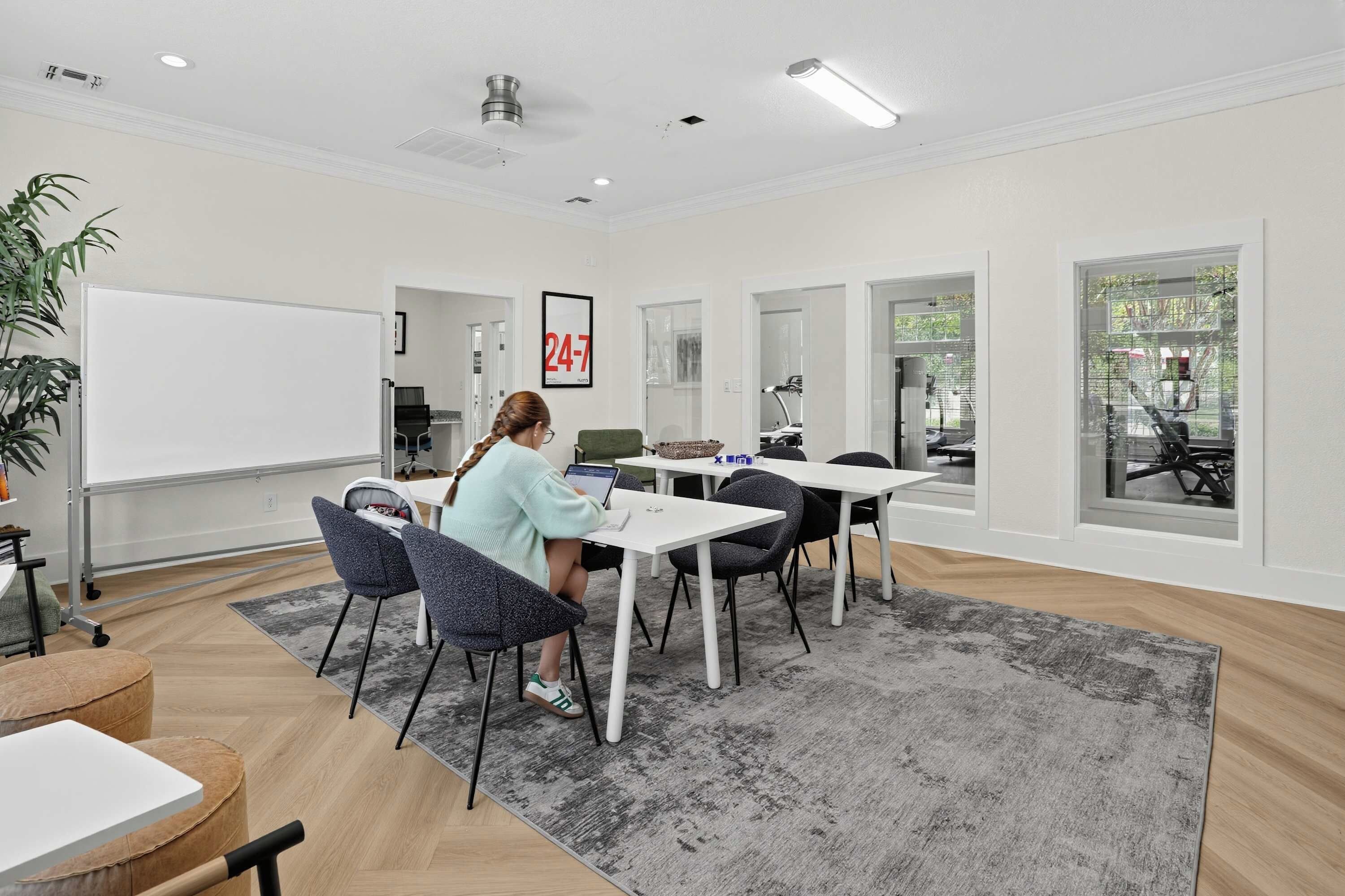 A modern office space with a whiteboard, a 24/7 sign, and a large window with a view of a car.