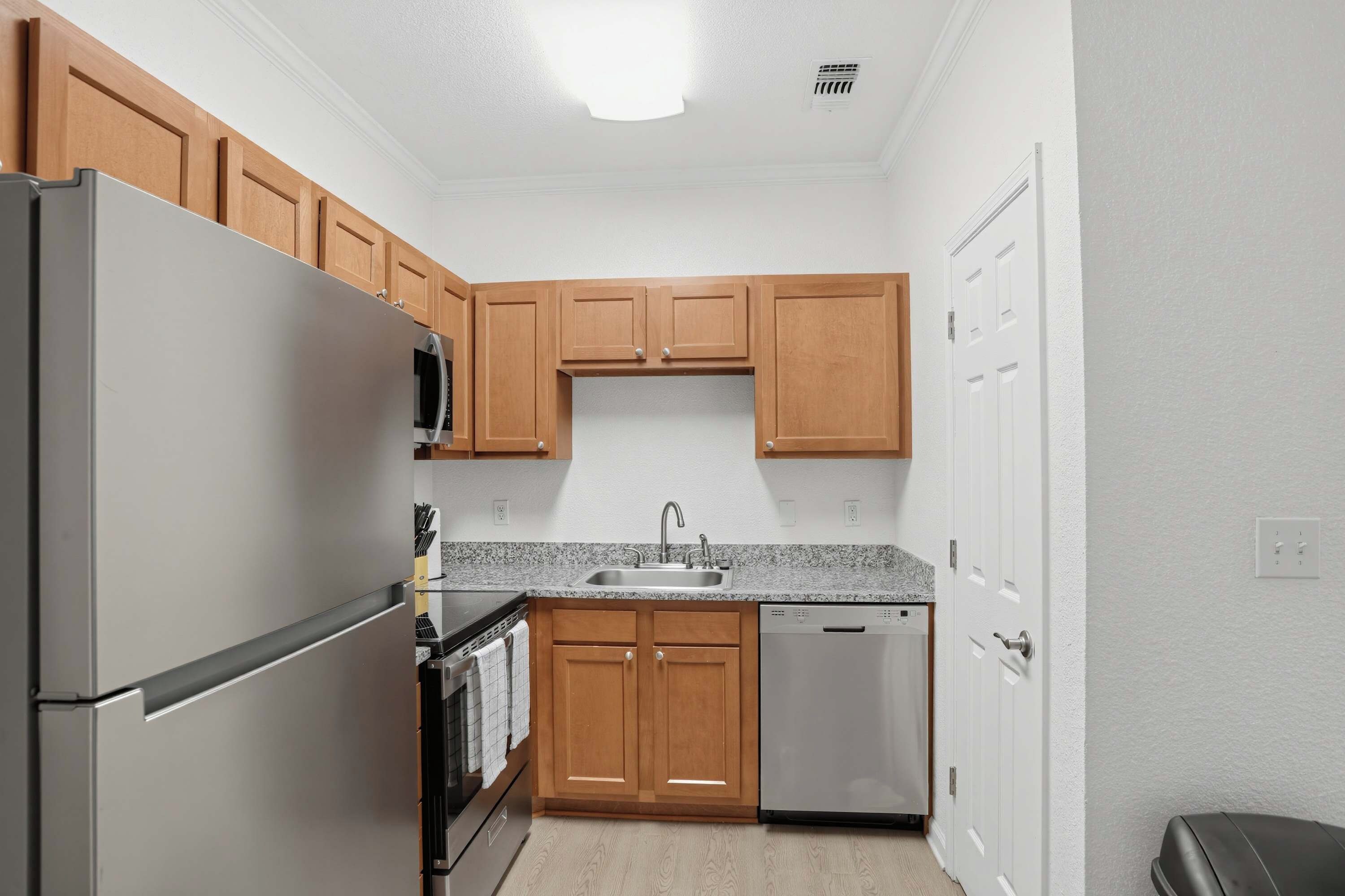 Una cocina compacta con un refrigerador de acero inoxidable, un microondas, un lavamanos, armarios de madera y un lavavajillas.