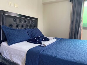 A bed with a tufted headboard, two pillows, a folded blanket, and a blue quilted bedspread. - Modern apartment in Gazcue, near the Zona Colonial - Malecón (Santo Domingo)