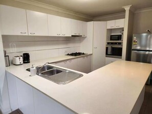 Una cocina moderna con armarios blancos, un lavamanos de acero inoxidable, horno empotrado y refrigerador.
