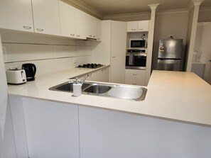 Eine moderne Küche mit weißen Schränken, einer Edelstahl-Spüle, einem Gasherd, einer Mikrowelle, einem Backofen und einem Kühlschrank.
