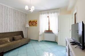 A living room with a sofa, a television, a radiator, and a window with curtains. - Villa Sinfonia, Exclusive Villa in Ravello (Ravello)