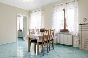 A dining area with a table set for two, wooden chairs, a potted plant, and a window with curtains. - Villa Sinfonia, Exclusive Villa in Ravello (Ravello)
