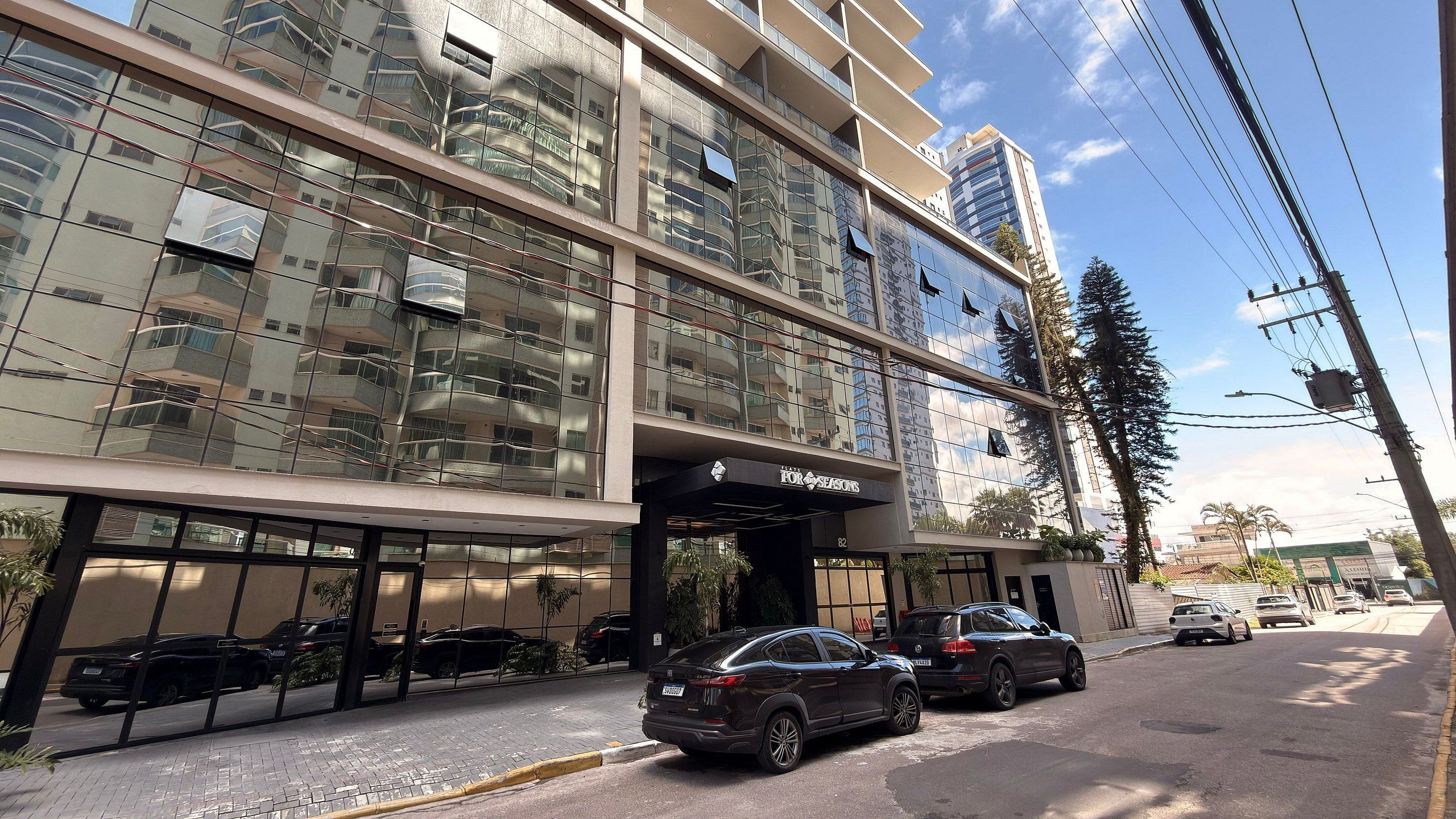 A multi-story hotel with a glass facade, parked cars, and a clear sky.