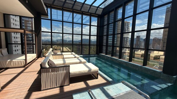 A modern indoor pool area with a clear view of the cityscape through large windows. - Flats For Seasons (Itapema)