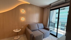 A modern room with a sofa, a small round table, and two wall-mounted lights. - Flats For Seasons (Itapema)