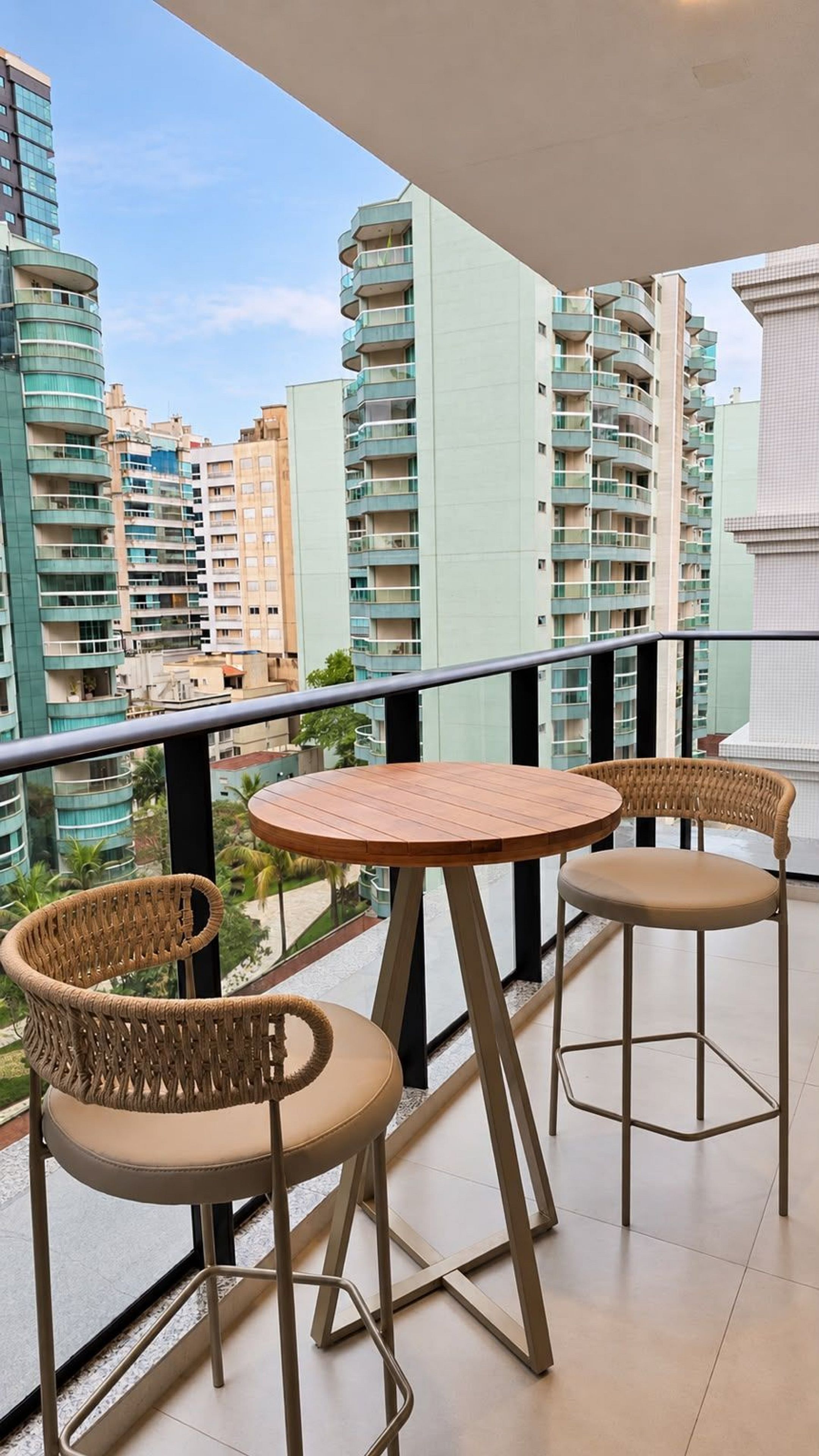 Un balcó amb dues cadires de vimetlina i una taula petita rodona, amb vista a un paisatge urbà amb edificis moderns.